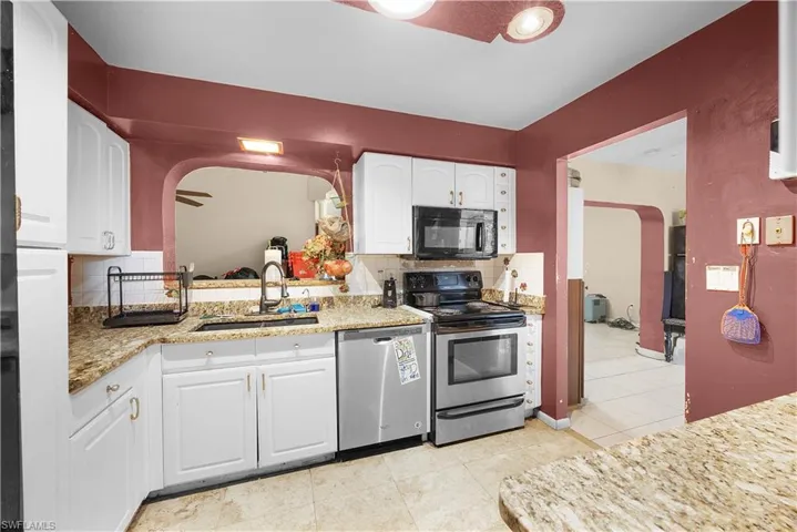 Kitchen with arched walkways, decorative backsplash, appliances with stainless steel finishes, light tile patterned floors, and white cabinetry