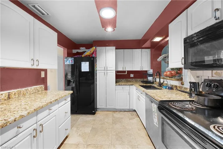 Kitchen with black appliances, white cabinetry, light stone countertops, and light tile patterned floors