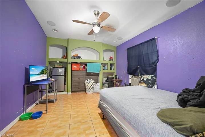 Bedroom featuring light tile patterned floors, freestanding refrigerator, and a ceiling fan