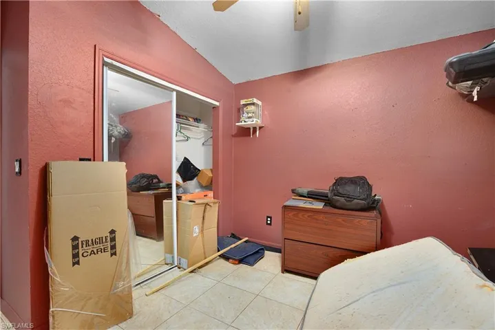 Bedroom featuring a textured wall, a closet, ceiling fan, lofted ceiling, and light tile patterned floors