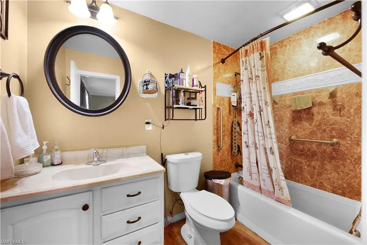 Full bathroom featuring shower / tub combo with curtain, vanity, and dark wood-type flooring