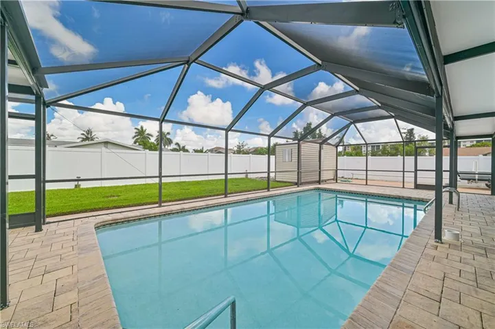 View of pool featuring glass enclosure, a fenced backyard, a sunroom, a shed, and patio surround