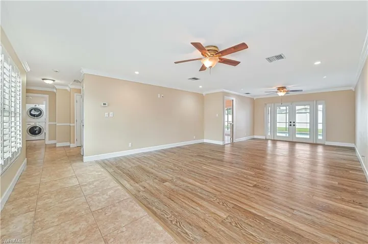 Spare room featuring ornamental molding, french doors, light wood-style floors, stacked washing machine and dryer, and ceiling fan