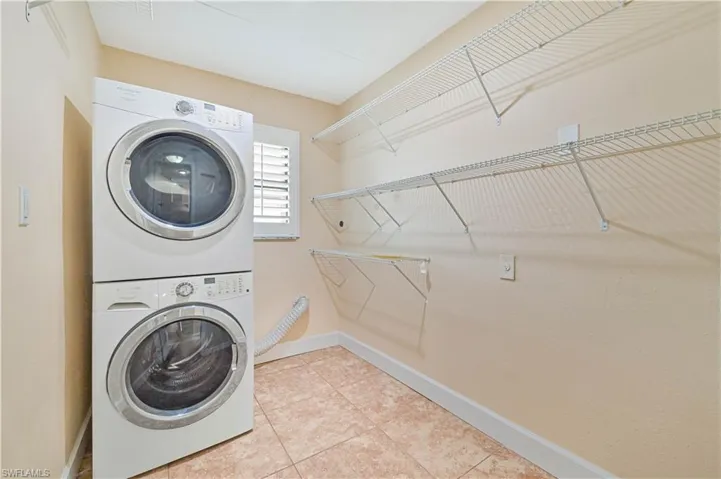 Laundry room with light tile patterned floors and stacked washing machine and dryer