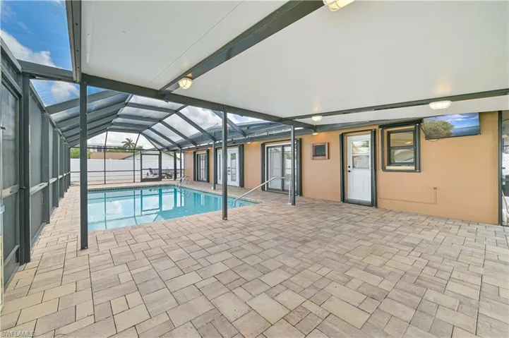 View of pool with glass enclosure, a sunroom, and patio surround