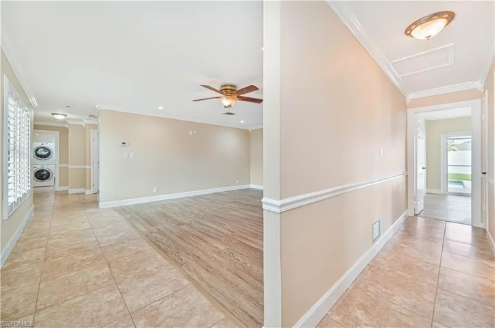 Corridor featuring light tile patterned flooring, crown molding, and stacked washer and dryer