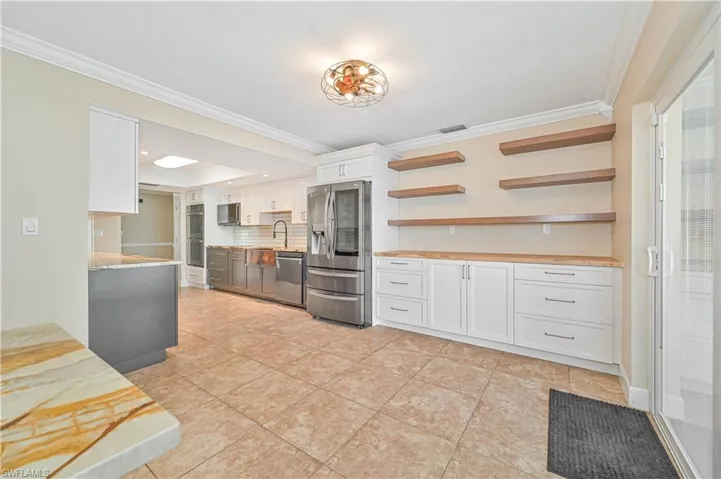 Dual tone kitchen featuring ornamental molding, open shelves, tasteful backsplash, stainless steel appliances, and two tone color scheme