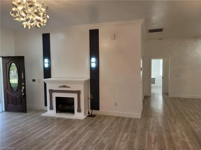 Unfurnished living room with ornamental molding, wood finished floors, and a chandelier