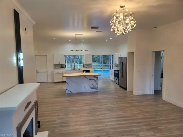 Kitchen with white cabinets, pendant lighting, an island with sink, appliances with stainless steel finishes, and crown molding