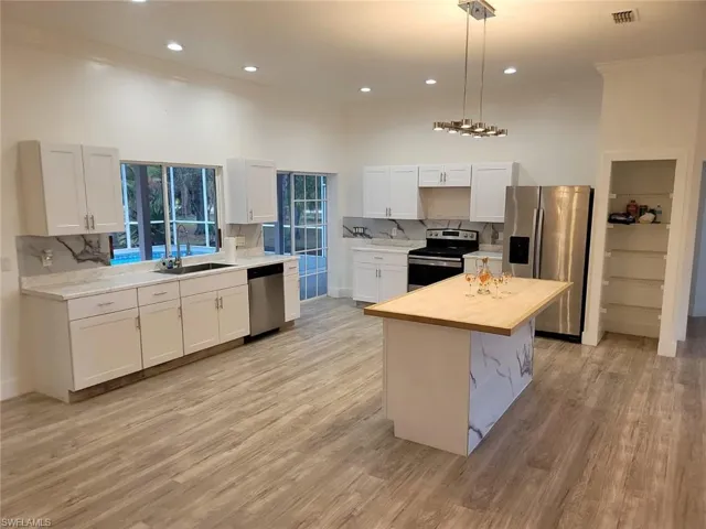 Kitchen featuring stainless steel appliances, white cabinets, light wood-type flooring, backsplash, and pendant lighting