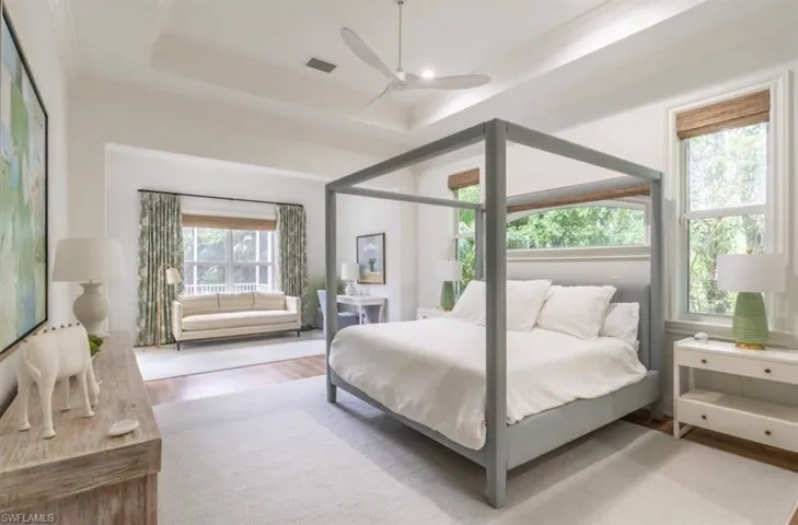 Bedroom with light wood finished floors, a ceiling fan, a tray ceiling, and crown molding