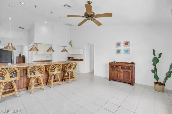 Tiled dining or den area with ceiling fan, sink, and high vaulted ceiling
