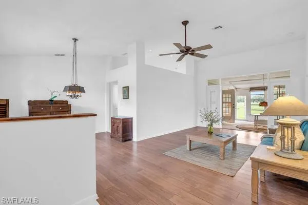 Living room with high vaulted ceiling, ceiling fan with notable chandelier, and wood-type flooring