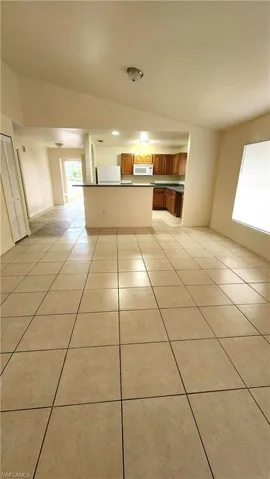 Kitchen featuring open floor plan, light tile patterned flooring, wood finish cabinetry, vaulted ceiling, and dark countertops