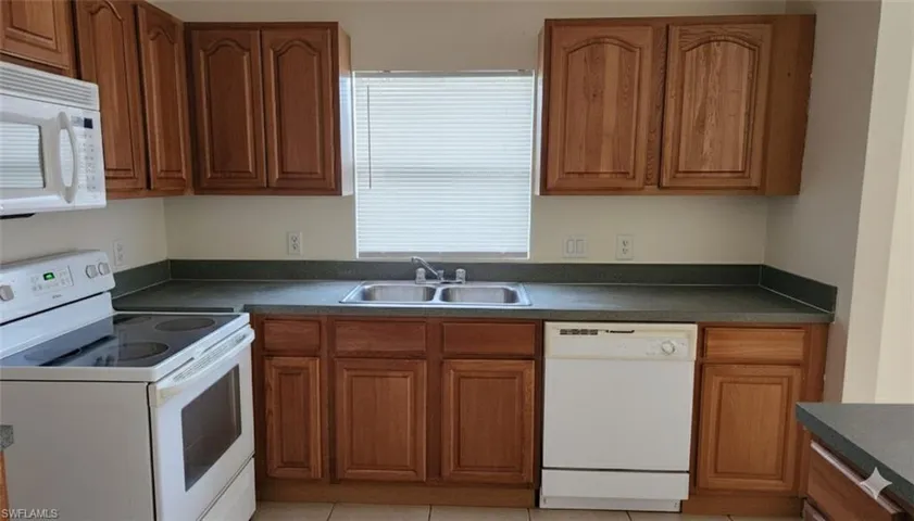 Kitchen featuring window, white appliances, wood finish cabinetry, dark countertops, and light tile patterned floors
