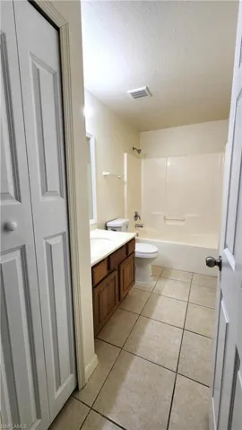 Bathroom featuring linen closet, vanity,  shower combination, light tile patterned floors, and a textured ceiling