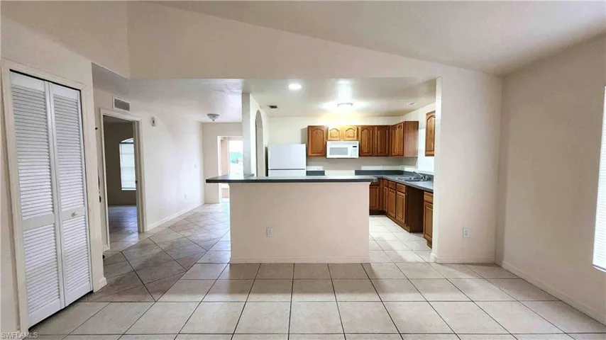 Kitchen with dark countertops, wood finish cabinetry, white appliances, lofted ceiling, and a center island