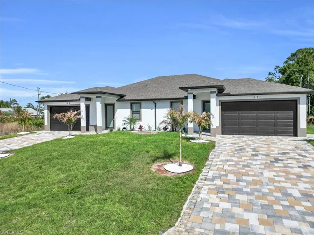 Prairie-style home featuring an attached garage, a front lawn, stucco siding, and driveway
