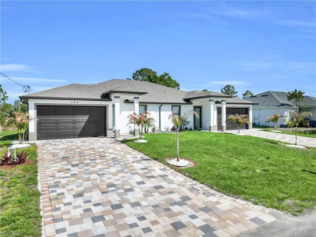 Prairie-style house featuring a front yard, a garage, decorative driveway, and stucco siding