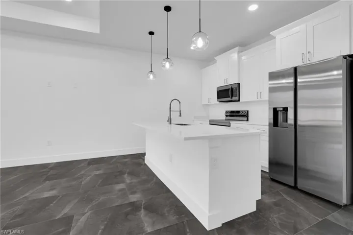 Kitchen with stainless steel appliances, white cabinets, an island with sink, pendant lighting, and light stone counters