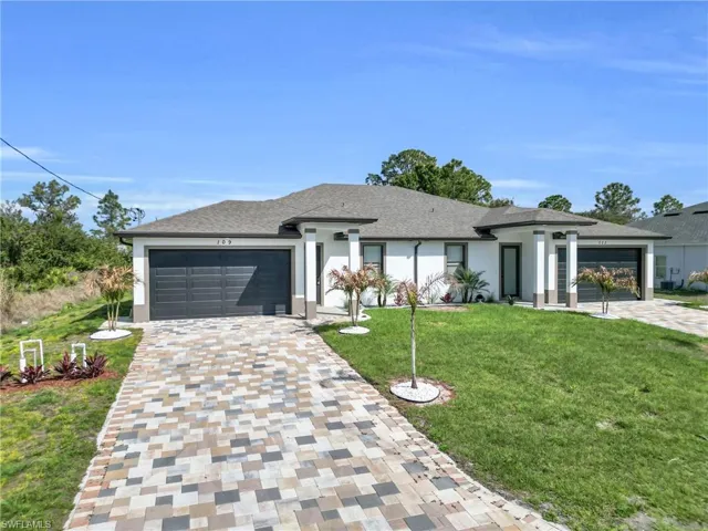 Prairie-style home featuring a front yard, a garage, decorative driveway, and stucco siding