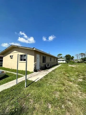 Single-story exterior featuring a light-toned stucco finish, partial stone-veneer cladding, a concrete walkway, and an open grass yard