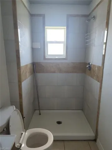Shower stall featuring white wall tile, decorative neutral stone accent inlay, single-handle shower valve, and a window