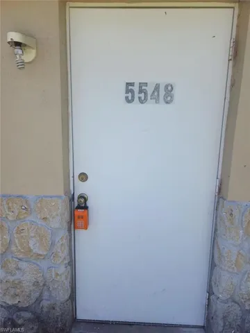 Solid white entry door featuring metallic address numerals, dual-lock hardware, and exterior stone-finish wainscoting