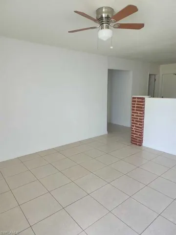 Neutral-tone ceramic tile flooring, a brick-accented pony wall, and a brushed metal ceiling fan with a glass globe light fixture