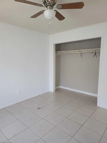 Room featuring tile flooring, ceiling fan with integrated light fixture, and a reach-in closet with built-in shelving