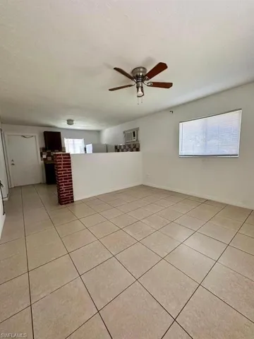 Open-concept interior featuring large-format ceramic tile flooring, a half-wall partition with a decorative brick column, and a central ceiling fan