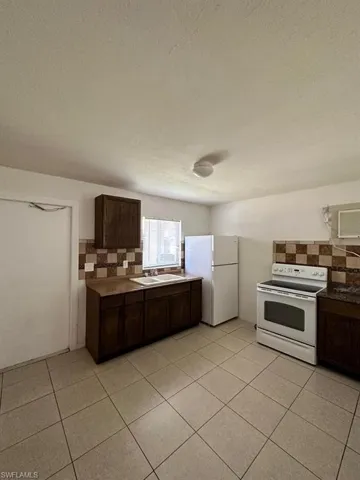 Kitchen featuring dark wood cabinetry, tile flooring, stone-finish countertops, tiled backsplash, and integrated appliances