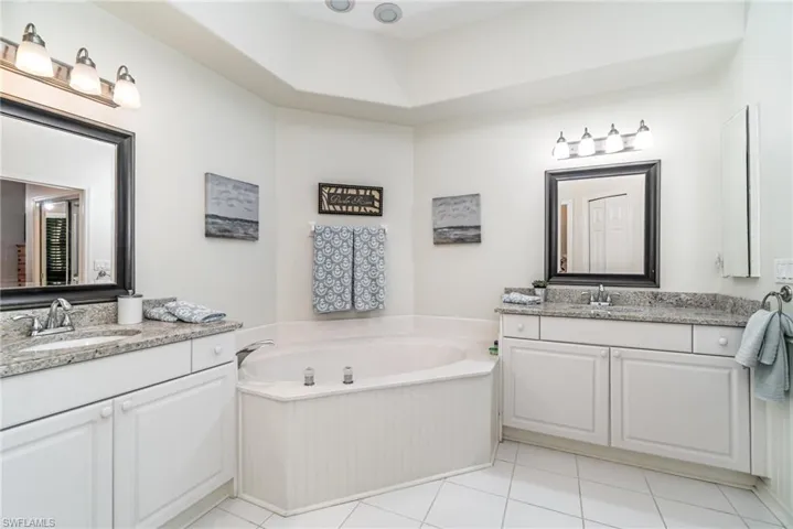 Bathroom featuring a bath, two vanities, and light tile patterned floors