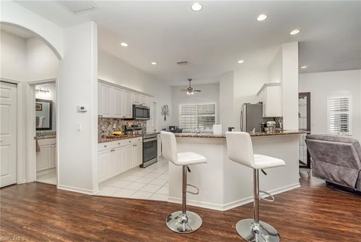 Kitchen featuring arched walkways, appliances with stainless steel finishes, a kitchen breakfast bar, dark stone counters, and recessed lighting