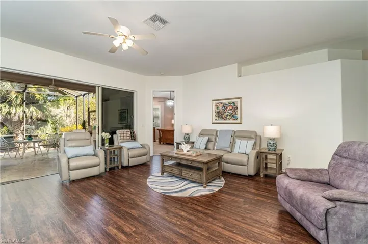Living area with dark wood-style floors, ceiling fan, and a sunroom