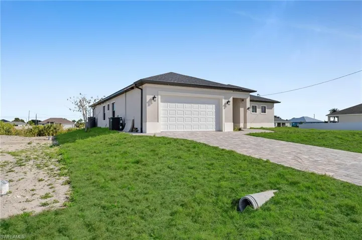 View of property exterior featuring decorative driveway, a lawn, a garage, and stucco siding