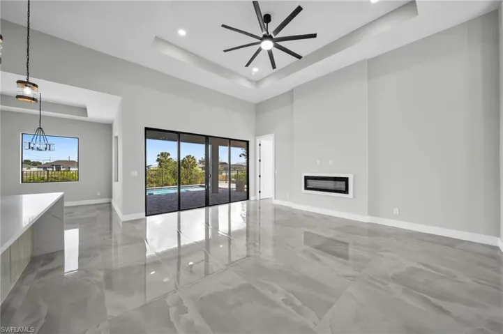 Unfurnished living room with a glass covered fireplace, a ceiling fan, recessed lighting, light marble finish flooring, and a high tray ceiling