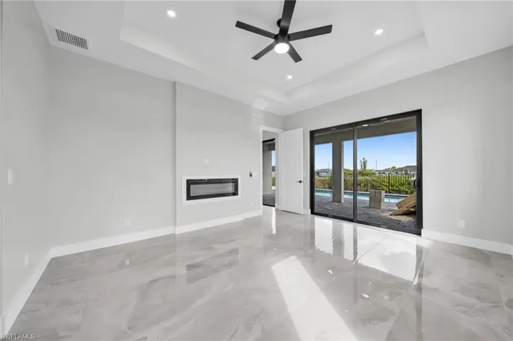 Unfurnished living room with a glass covered fireplace, a ceiling fan, a raised ceiling, and recessed lighting