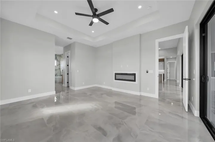 Unfurnished living room with a glass covered fireplace, ceiling fan, recessed lighting, and a tray ceiling