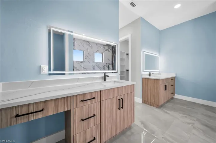Bathroom featuring two vanities, a marble finish shower, and light marble finish floors