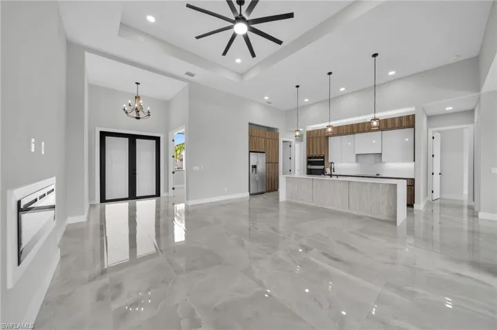 Unfurnished living room with a ceiling fan, a tray ceiling, light marble finish flooring, a chandelier, and french doors