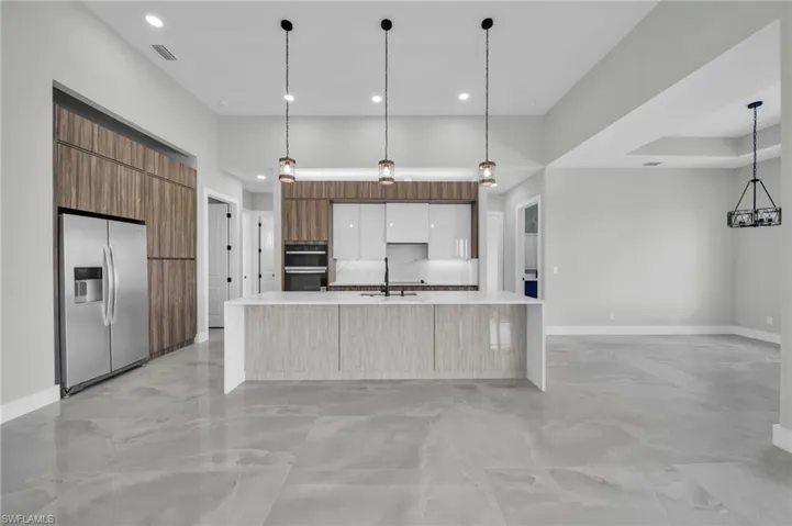 Kitchen featuring stainless steel fridge with ice dispenser, pendant lighting, a large island, modern cabinets, and a high ceiling
