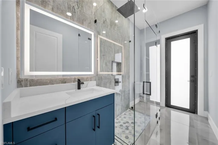 Full bath featuring a marble finish shower, vanity, tile walls, and light tile patterned flooring