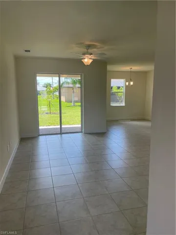 Unfurnished room featuring ceiling fan with notable chandelier, a wealth of natural light, and light tile patterned floors