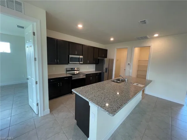 Kitchen featuring stainless steel appliances, sink, light tile patterned floors, and a kitchen island with sink