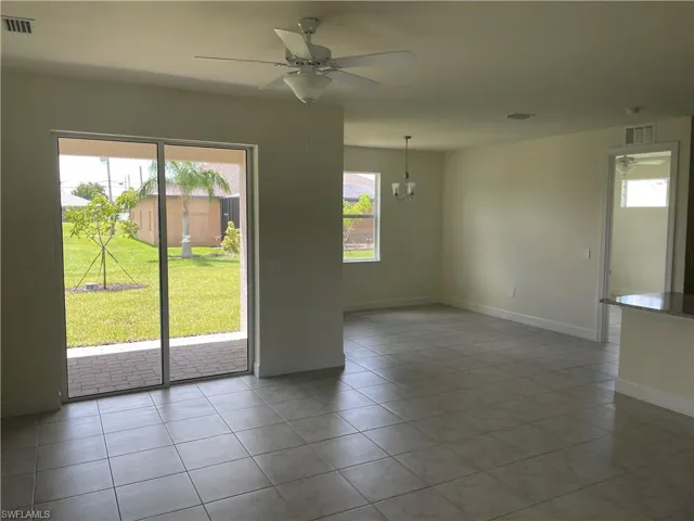Tiled empty room featuring ceiling fan with notable chandelier