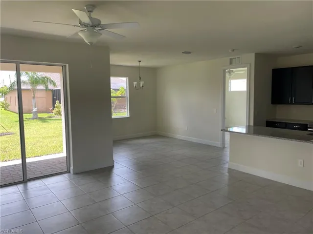 Unfurnished living room with ceiling fan with notable chandelier and light tile patterned flooring
