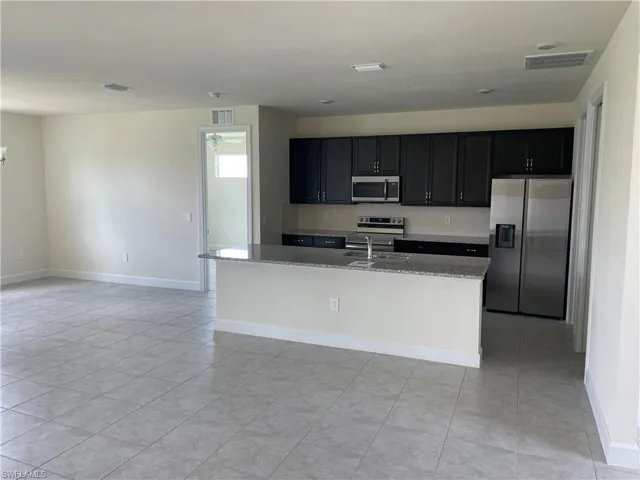 Kitchen featuring light tile patterned floors, light stone counters, stainless steel appliances, sink, and a kitchen island with sink