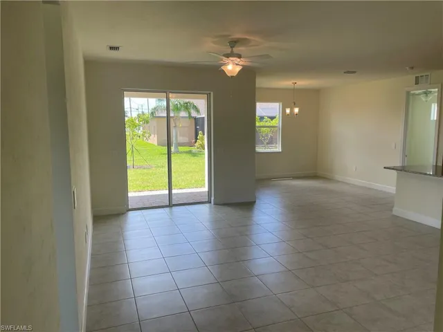 Empty room with a wealth of natural light, ceiling fan with notable chandelier, and light tile patterned floors