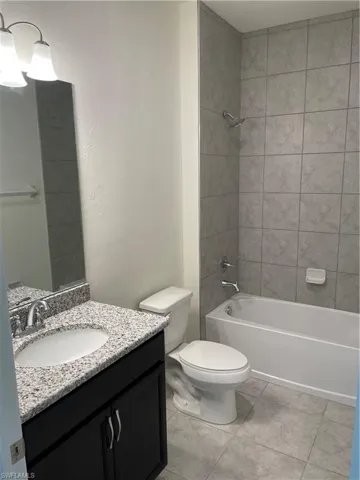 Full bathroom with tile patterned flooring, toilet, tiled shower / bath combo, and vanity